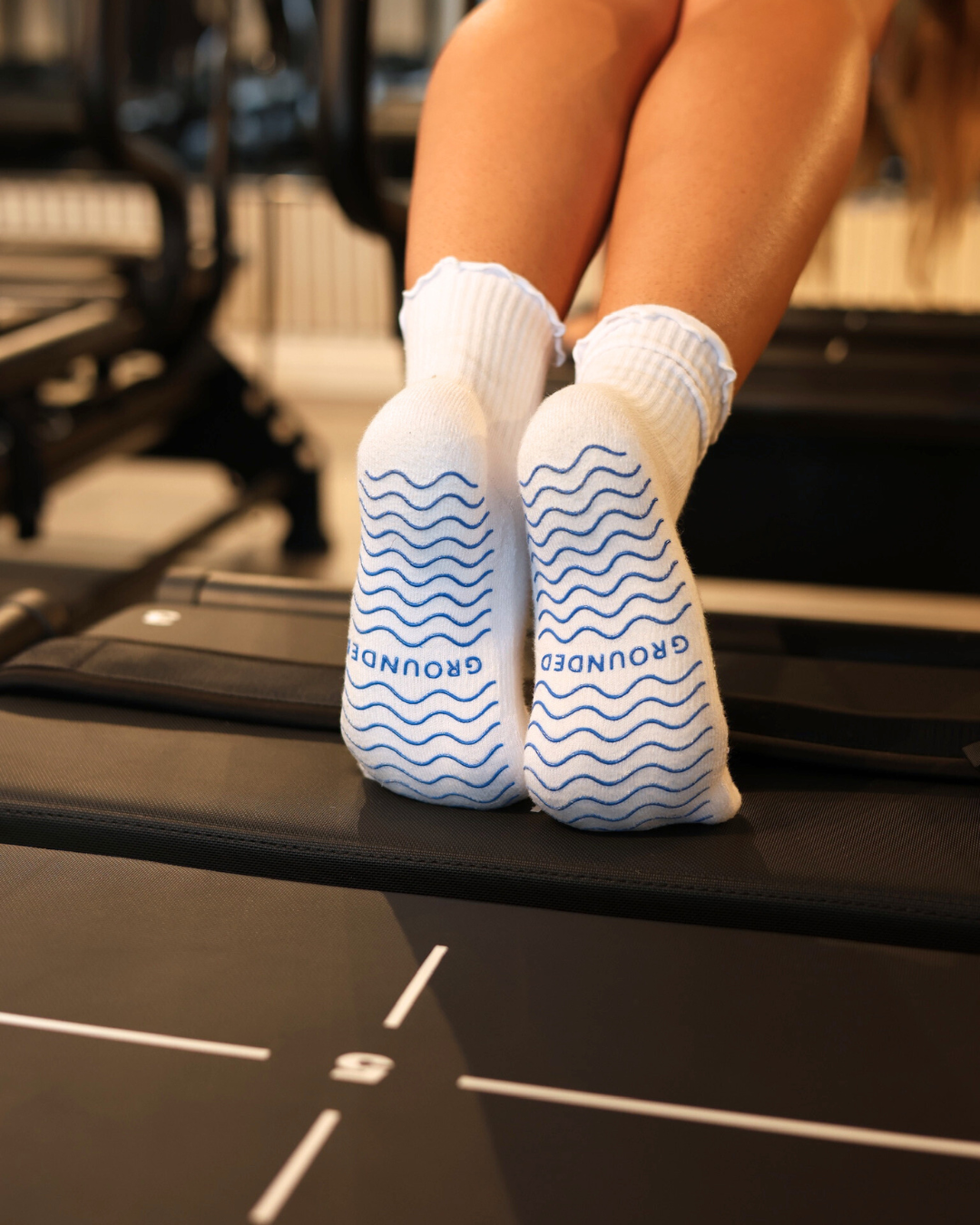 Person wearing white pilates socks with blue patterns on a pilates reformer