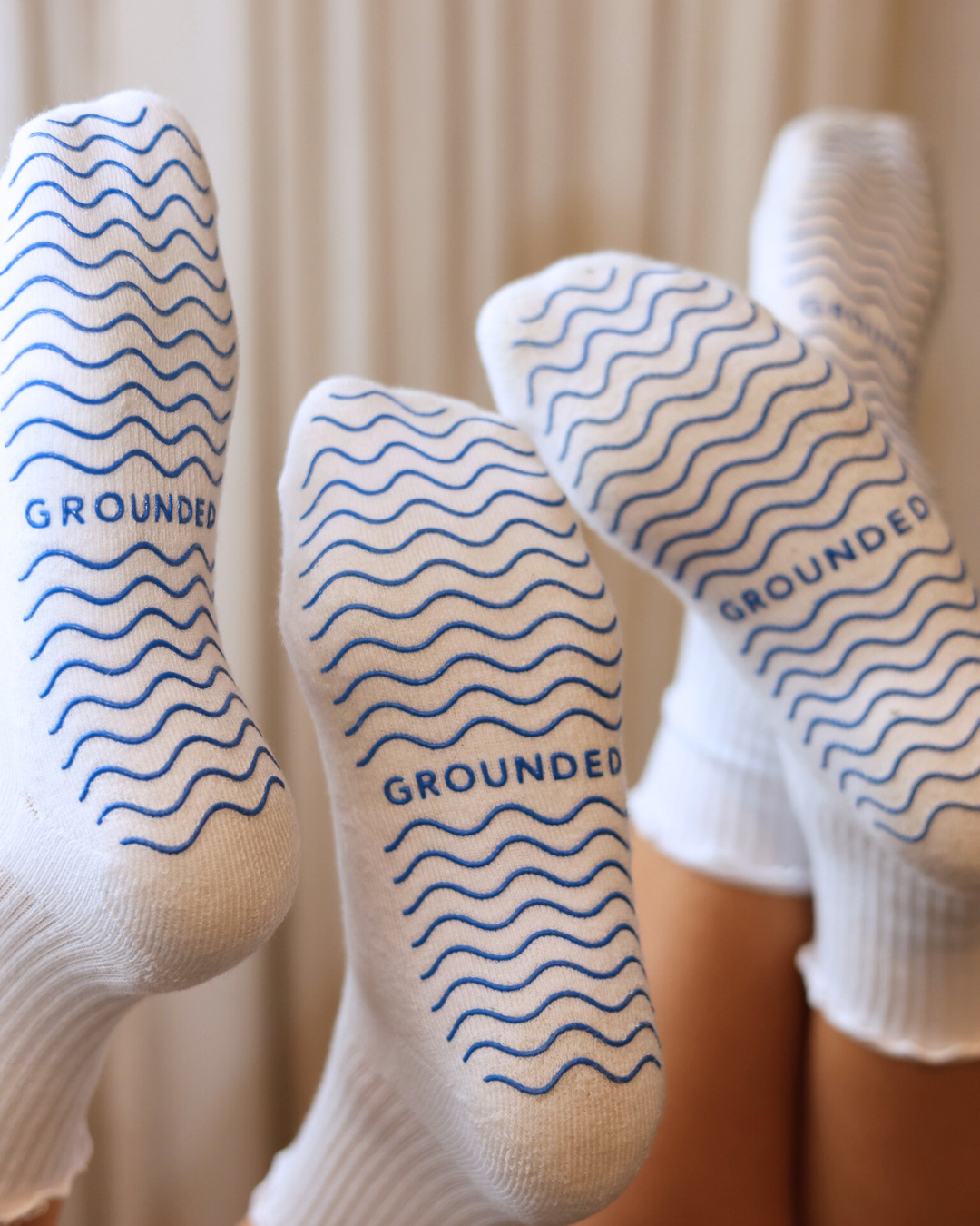 White barre socks with blue patterns and 'GROUNDED' text on a neutral background