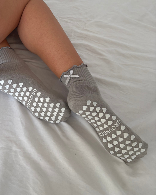 Grey frilly grip socks with white textured sole on a light grey background