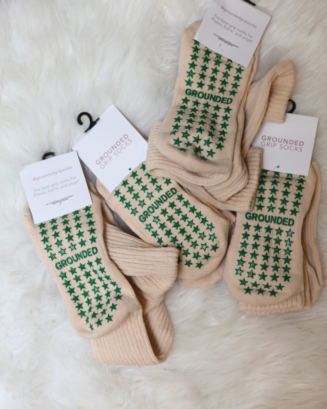 Beige socks with green star patterns and 'Grounded' text on a white background