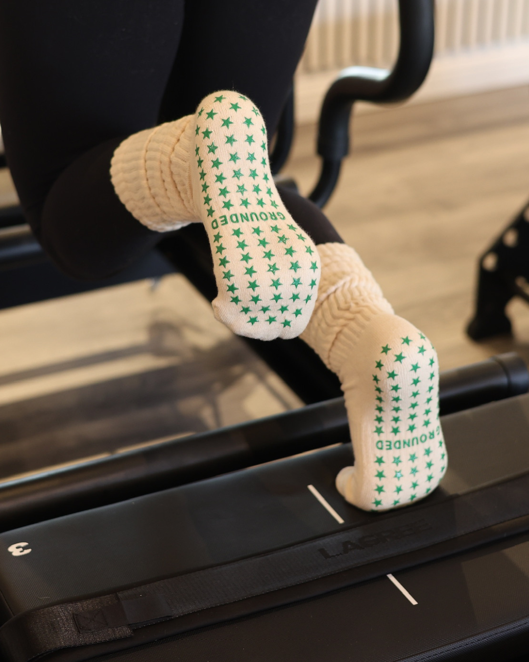 Beige Pilates grip socks with green star patterns on a Lagree reformer