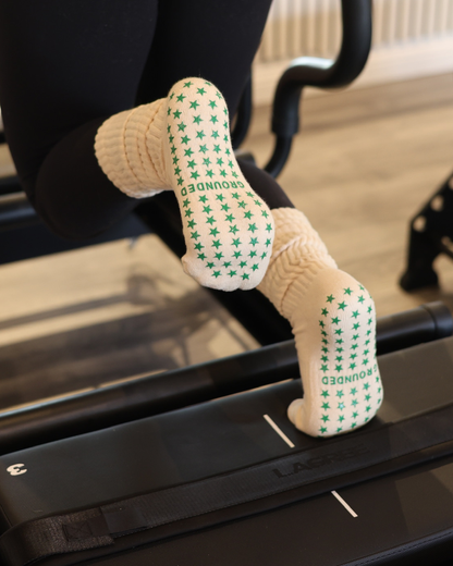 Beige Pilates grip socks with green star patterns on a Lagree reformer