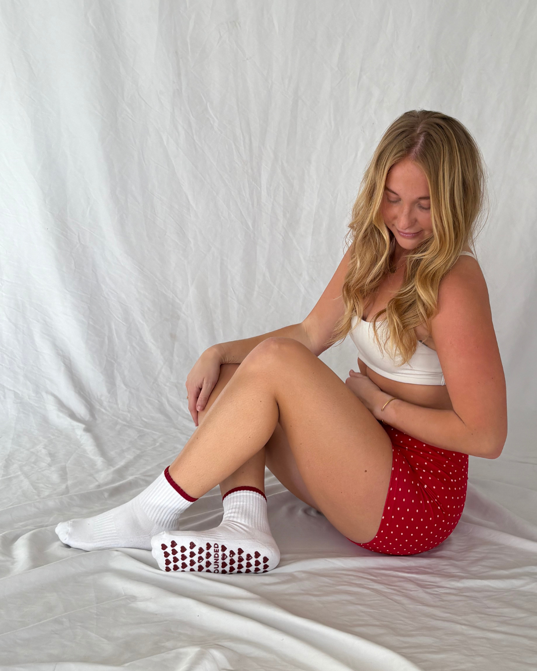 Woman sitting wearing white barre socks with red patterns and a red polka dot shorts.