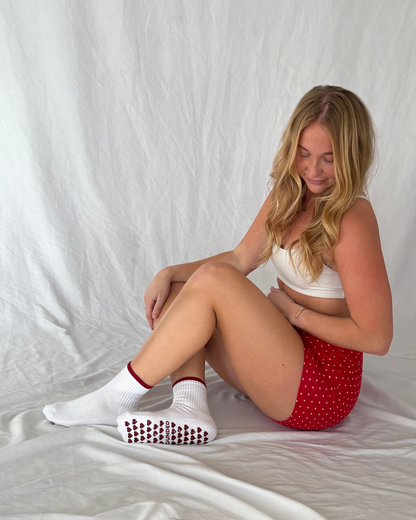 Woman sitting wearing white barre socks with red patterns and a red polka dot shorts.