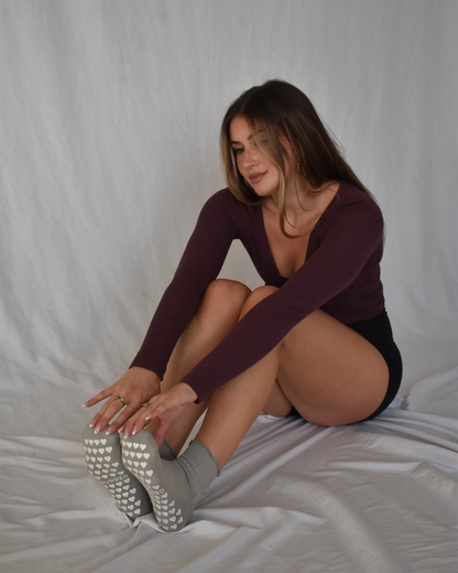 Woman sitting wearing a maroon long-sleeve top and black shorts and grey grippy socks