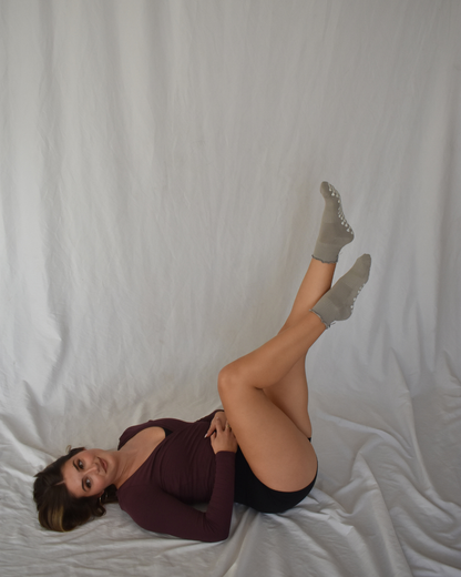 Woman lying down wearing a dark top and light-coloredruffle pilates socks