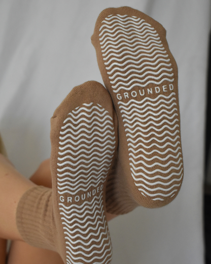 Close-up of brown barre socks with textured sole and 'GROUNDED' branding on a light background.