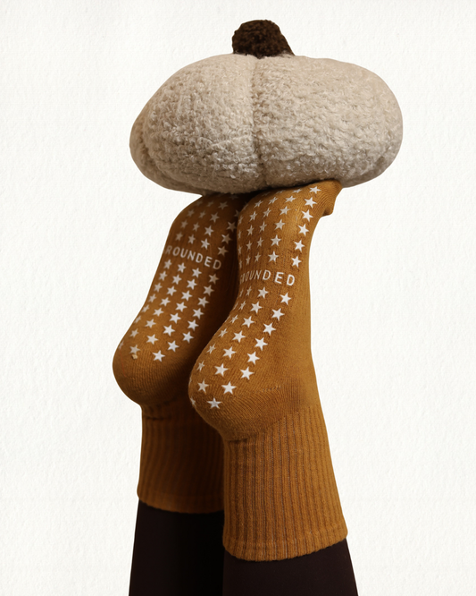 Person wearing pumpkin colored grip socks with a pumpkin balancing on their toes.