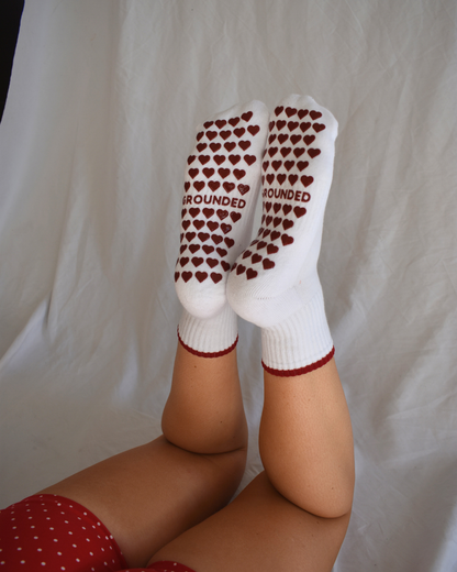 Grippy pilates socks with red heart patterns and 'Grounded' text on a plain background