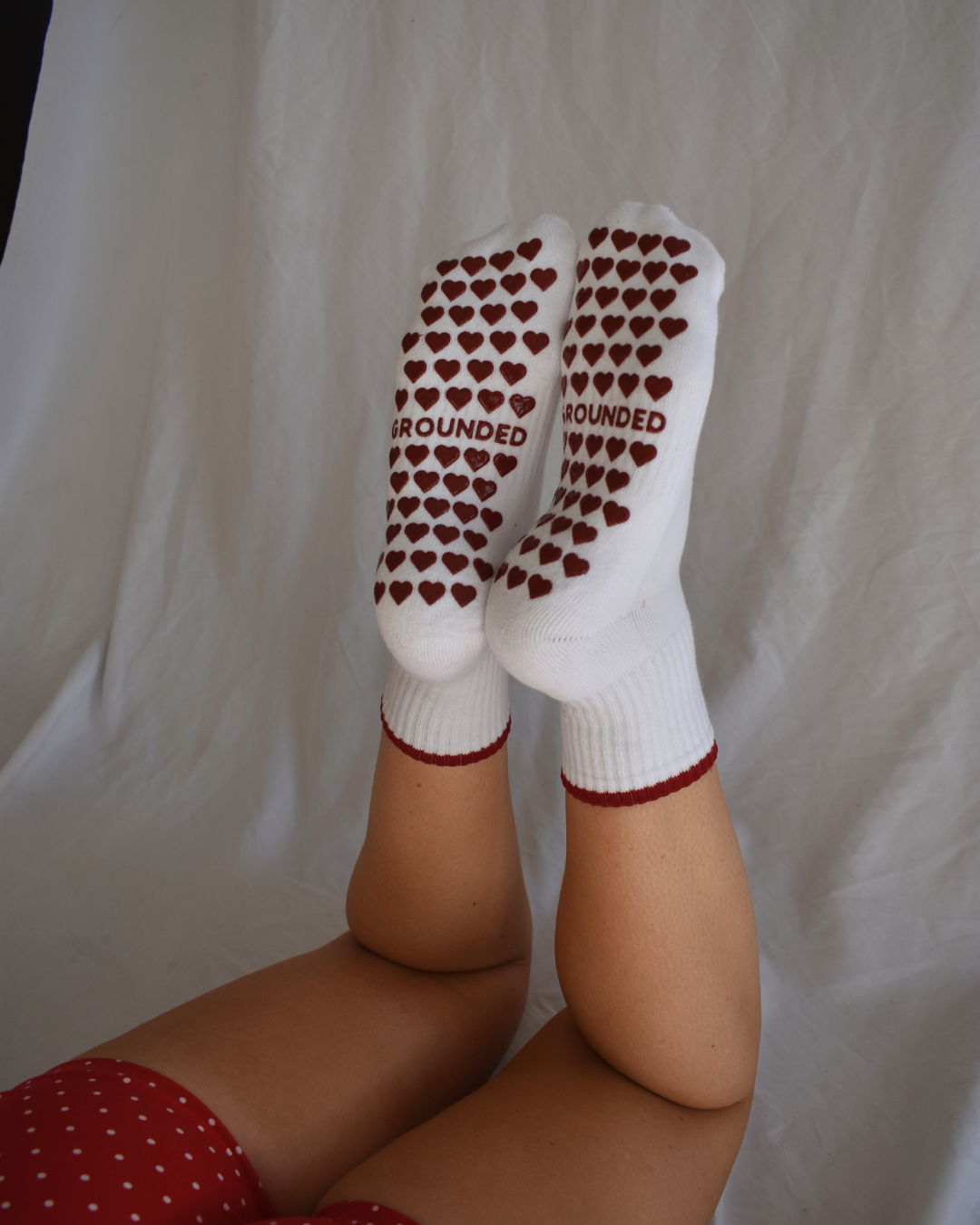 Grippy pilates socks with red heart patterns and 'Grounded' text on a plain background