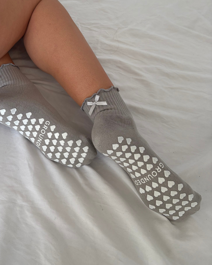 Grey frilly grip socks with white textured sole on a light grey background
