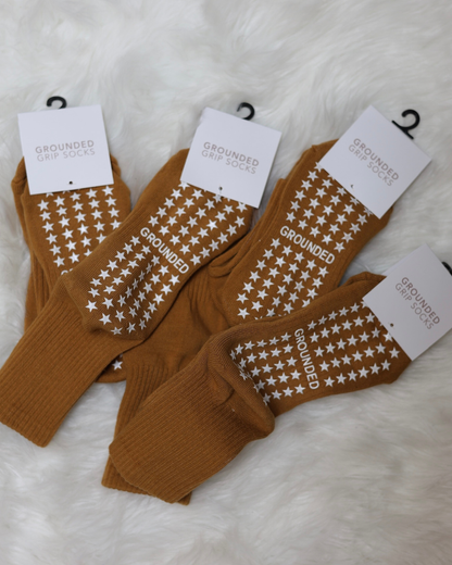 Mustard socks with star patterns and 'Grounded' text on white fluffy surface