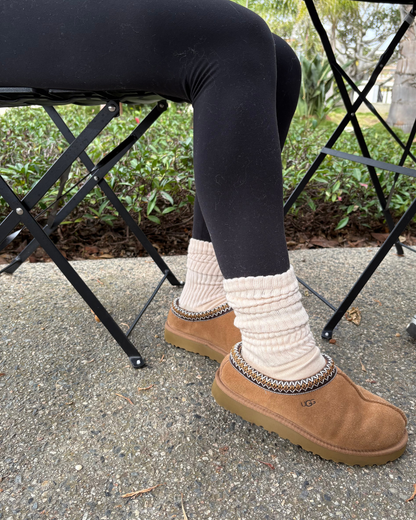 Person wearing brown UGG boots with beige scrunch socks sitting on a black metal chair outdoors.