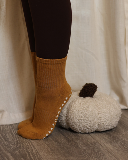 Pumpkin colored socks with star patterns worn by a person, with a white pumpkin and beige curtain in the background.
