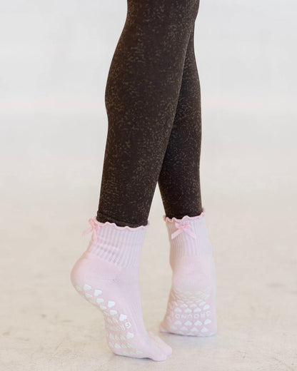 Pink pilates socks with bows socks worn with dark brown leggings on a light background