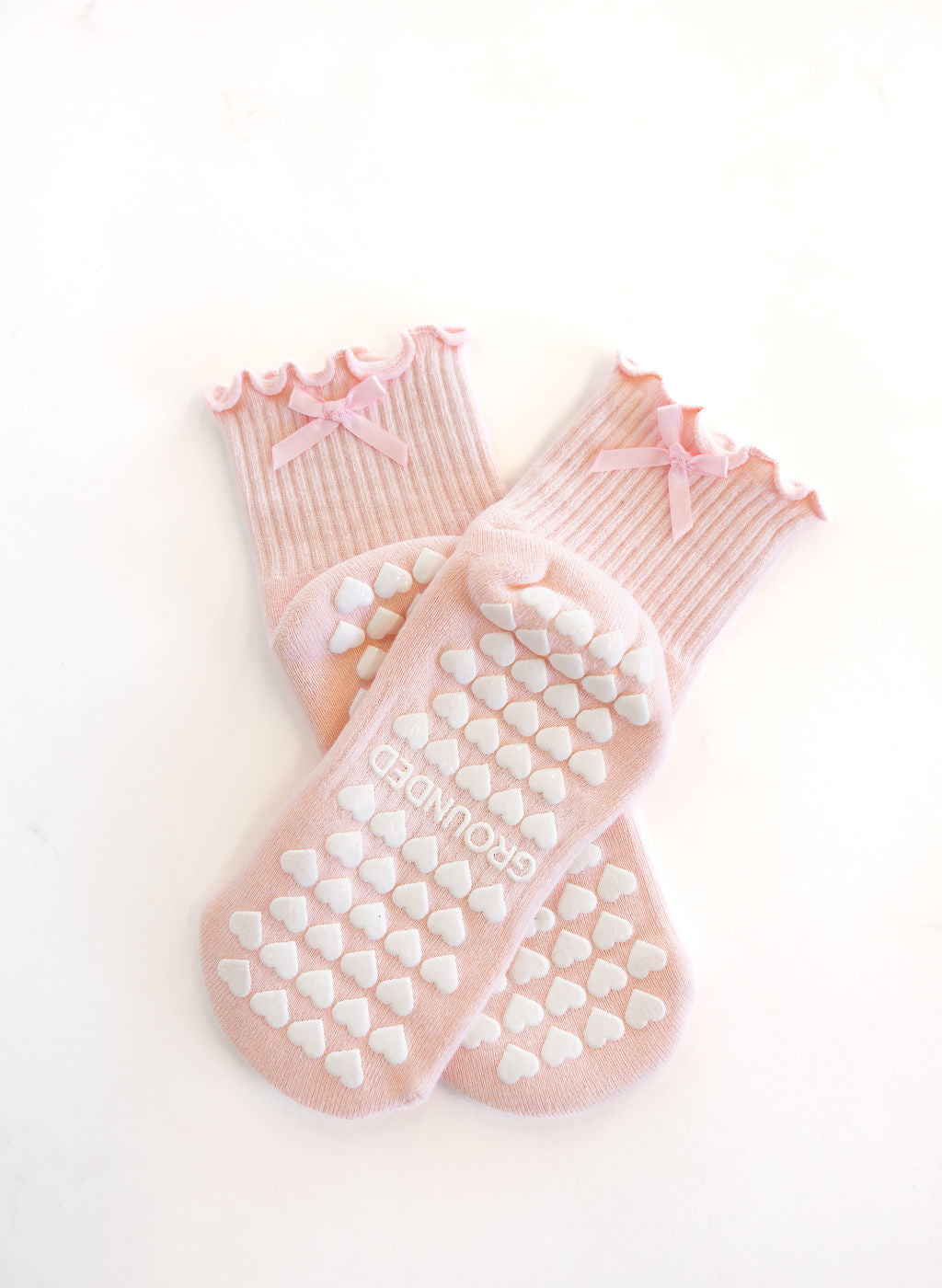 Pair of pink pilates socks with heart grips and bows on a white background