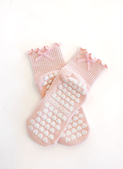 Pair of pink pilates socks with heart grips and bows on a white background
