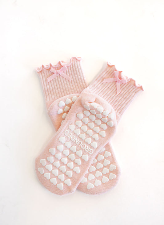Pair of pink pilates socks with heart grips and bows on a white background