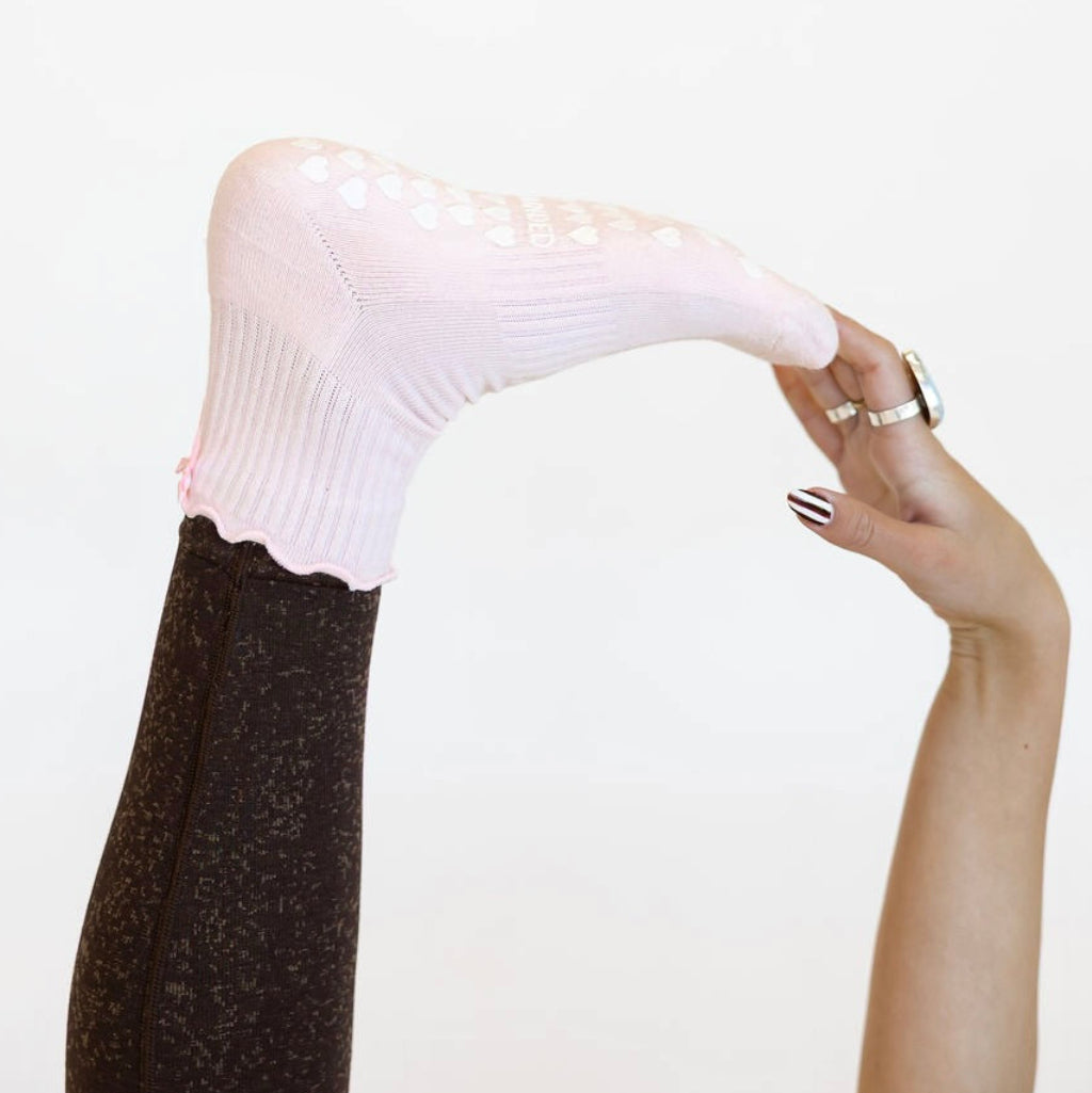 Person wearing a light pink grip sock and black tights on a plain background