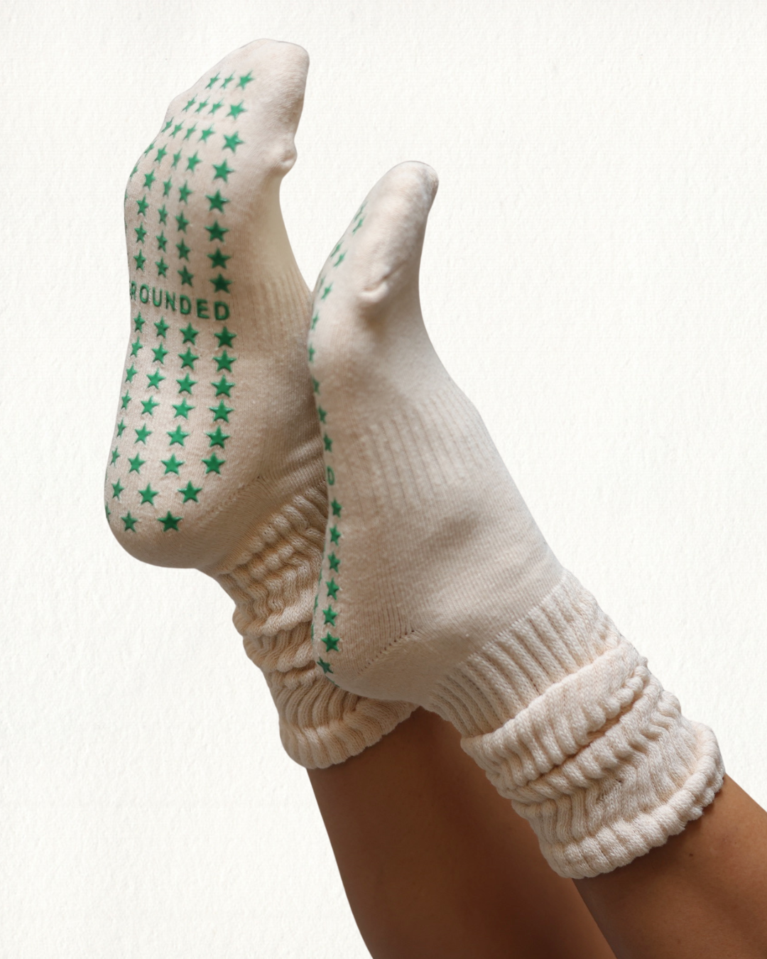 Beige grip socks with green star patterns and 'Grounded' branding on a white background